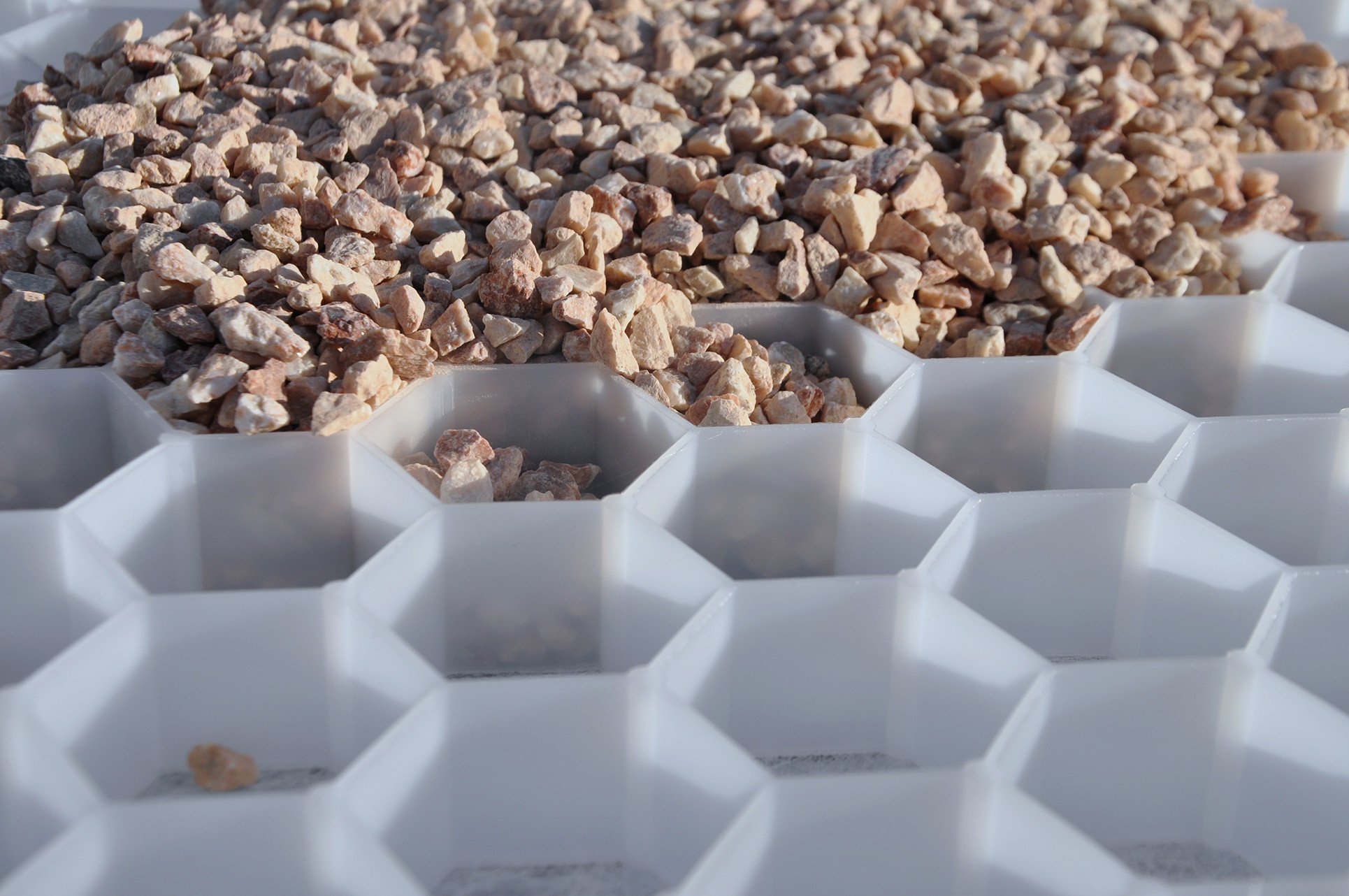 Primer plano de una rejilla de grava siendo rellenada con piedra para crear una superficie exterior duradera, estable y permeable.