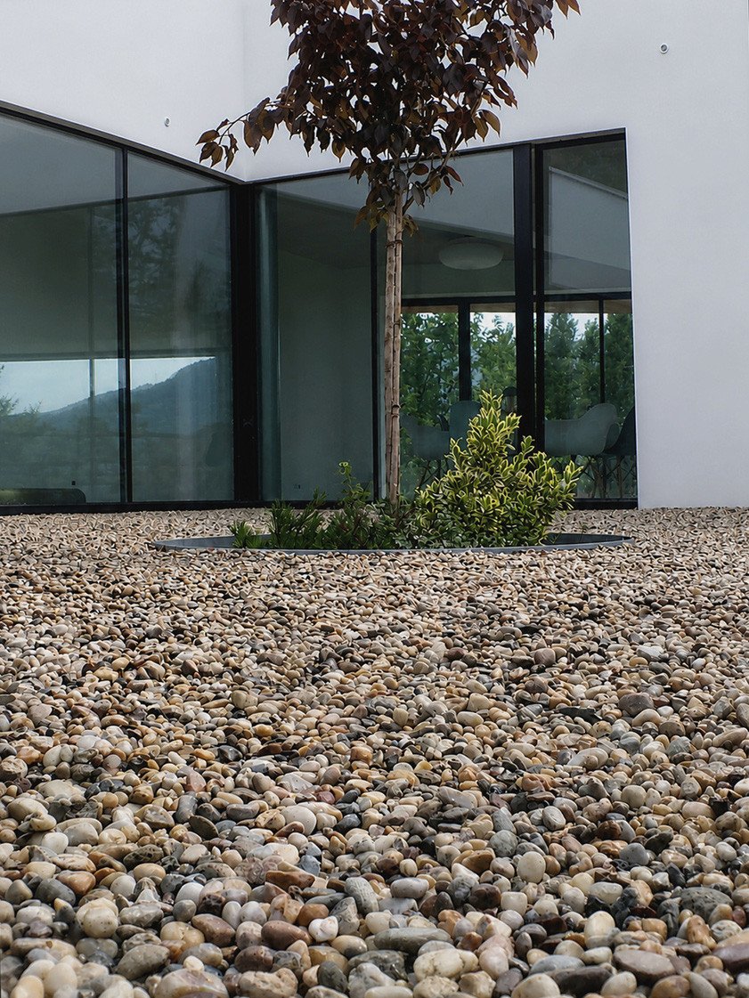 Una superficie de grava estable alrededor de una vivienda moderna combina un acabado cuidado con una infiltración eficaz del agua de lluvia.